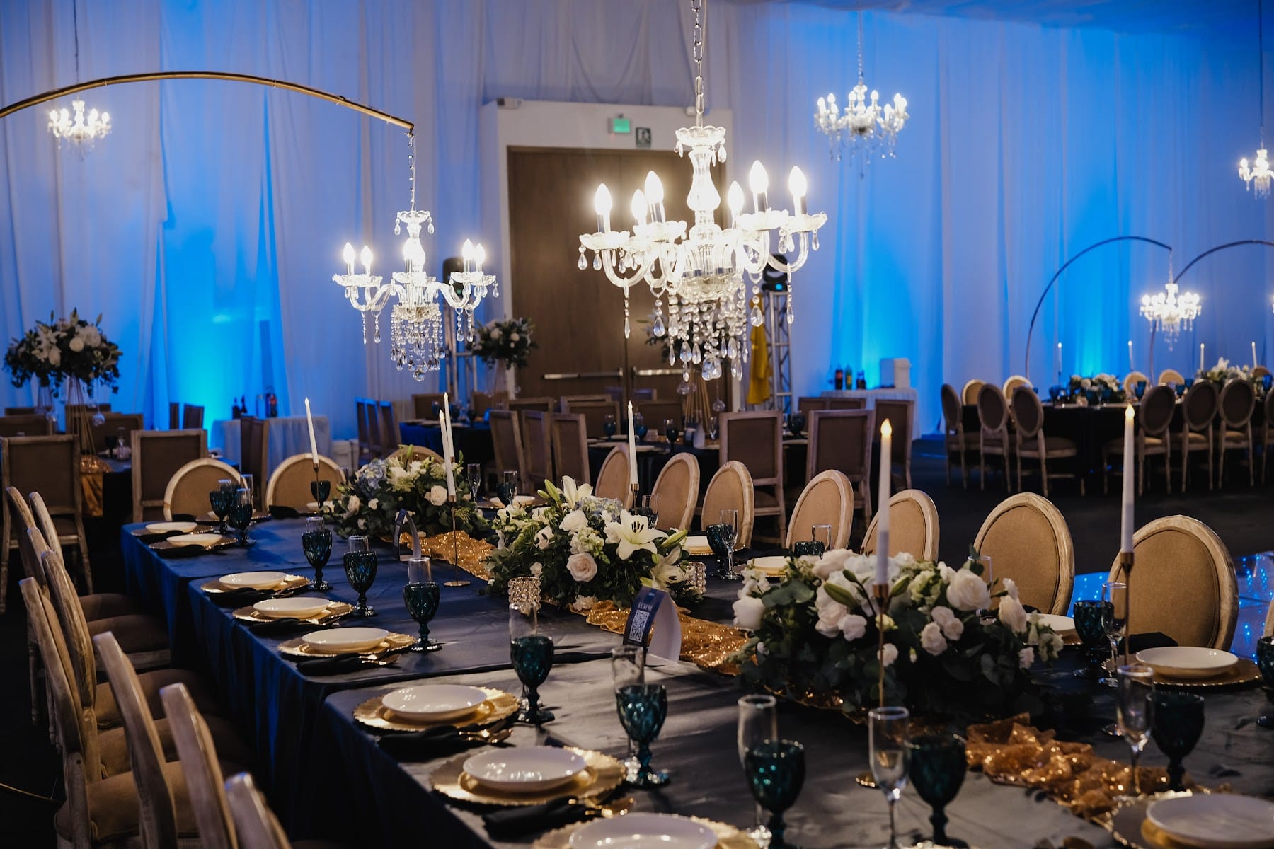 Escenario de boda con candil floral colgante, flores blancas y luz azul