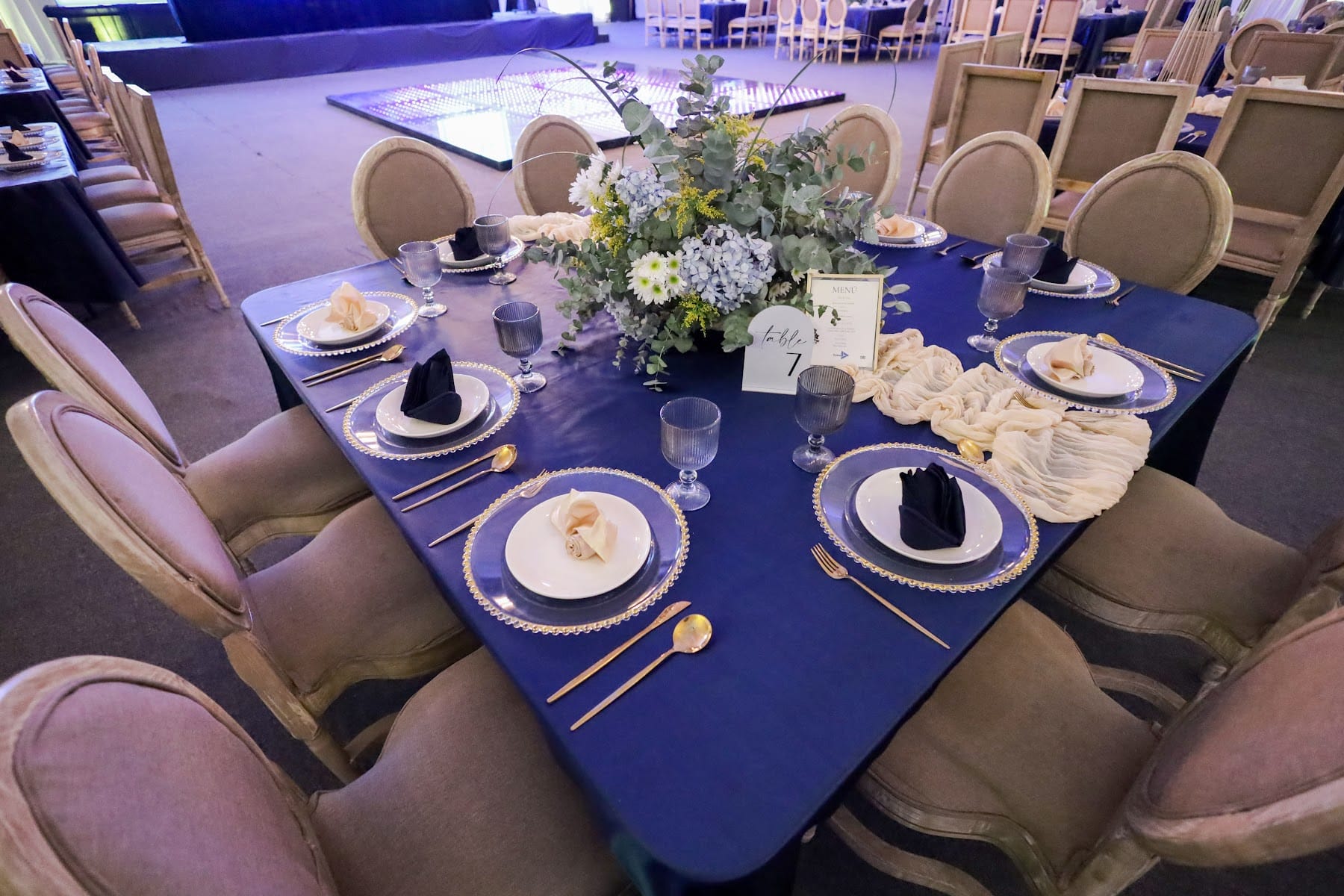 Mesa con mantel azul marino, vajilla y arreglo floral blanco