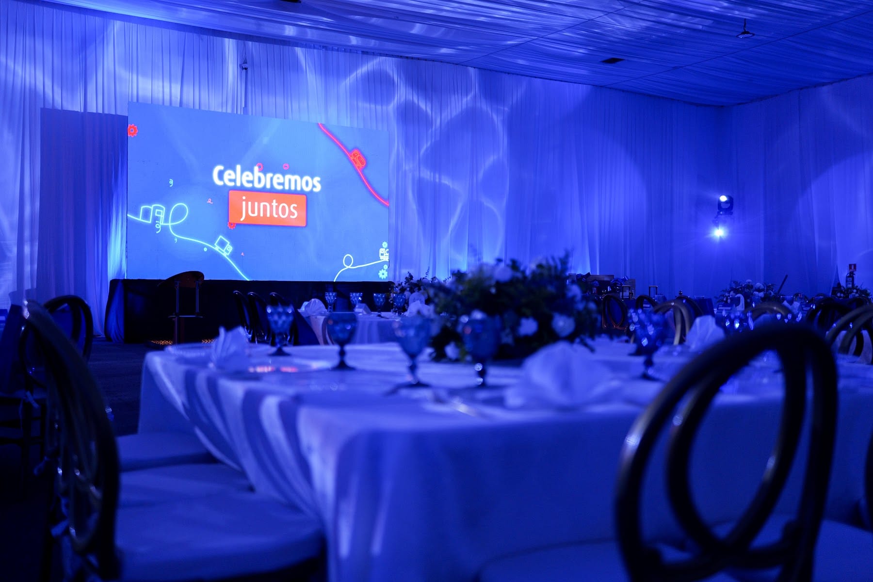 Montaje corporativo con mesas blancas y proyección azul en el salón