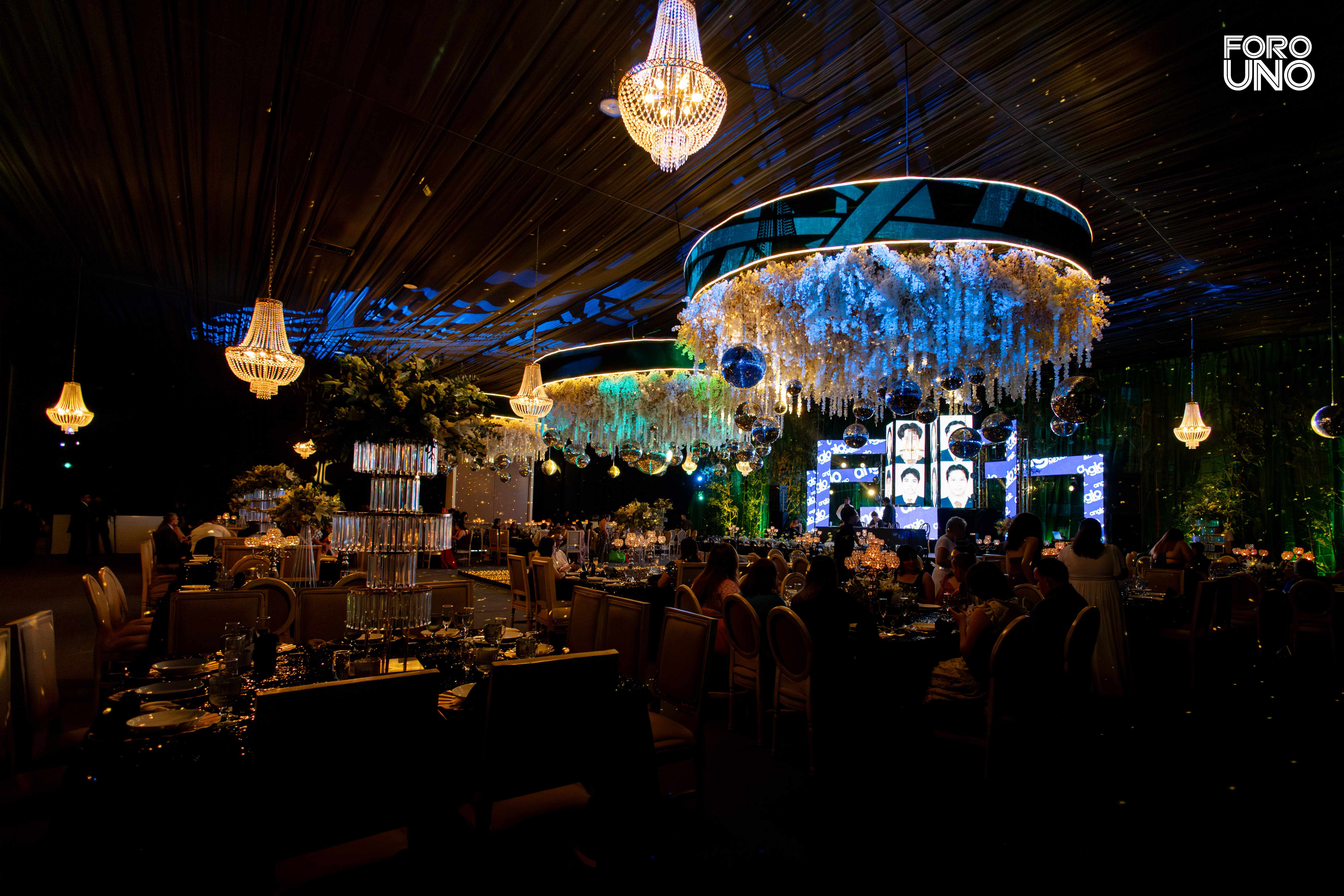 Invitados en una noche de celebración bajo candelabros y anillos florales iluminados