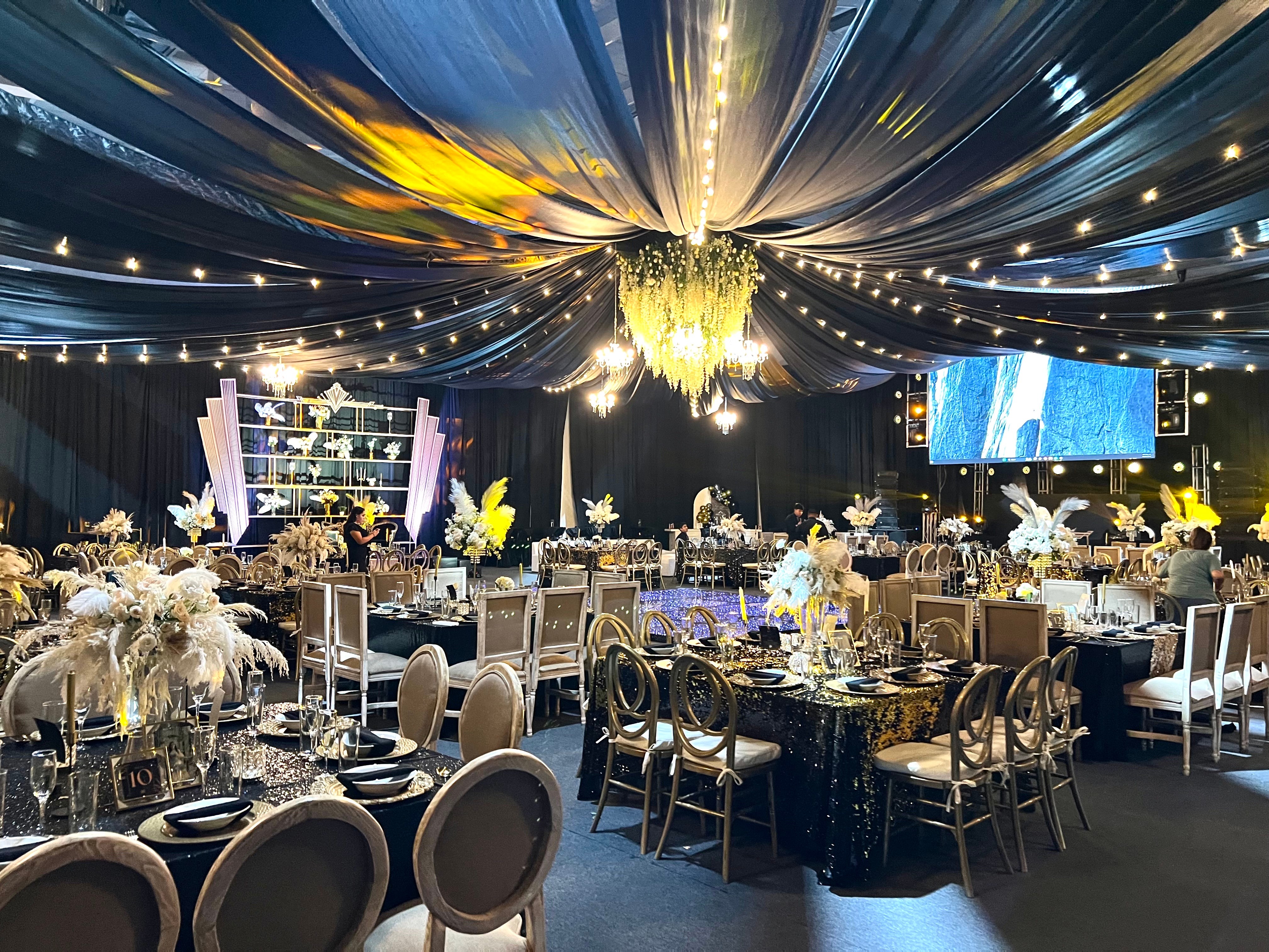 Gala de estilo art déco con techo de telas negras, luces colgantes y centros de plumas