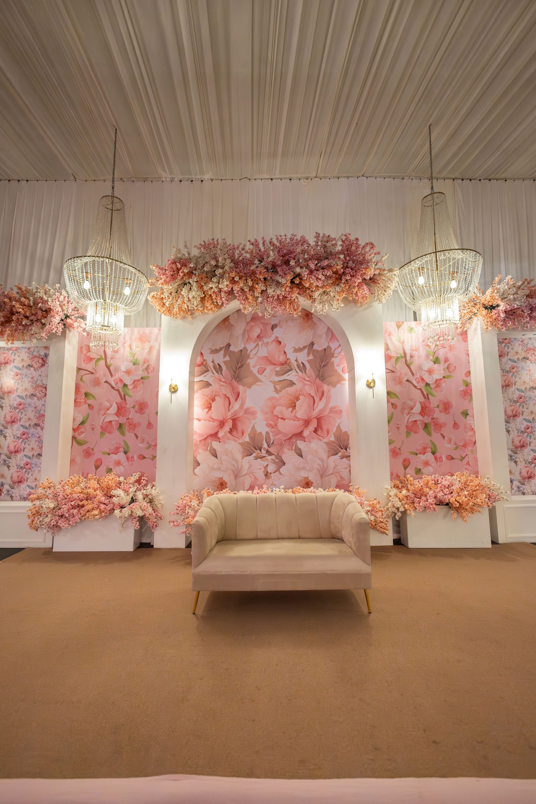 Escenario con arcos de murales florales rosas, candiles y sillón tapizado