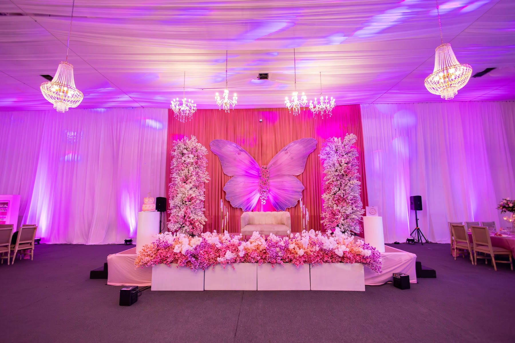 Escenario de XV años con mariposa monumental, columnas de flores, mesa principal floral y candelabros de cristal