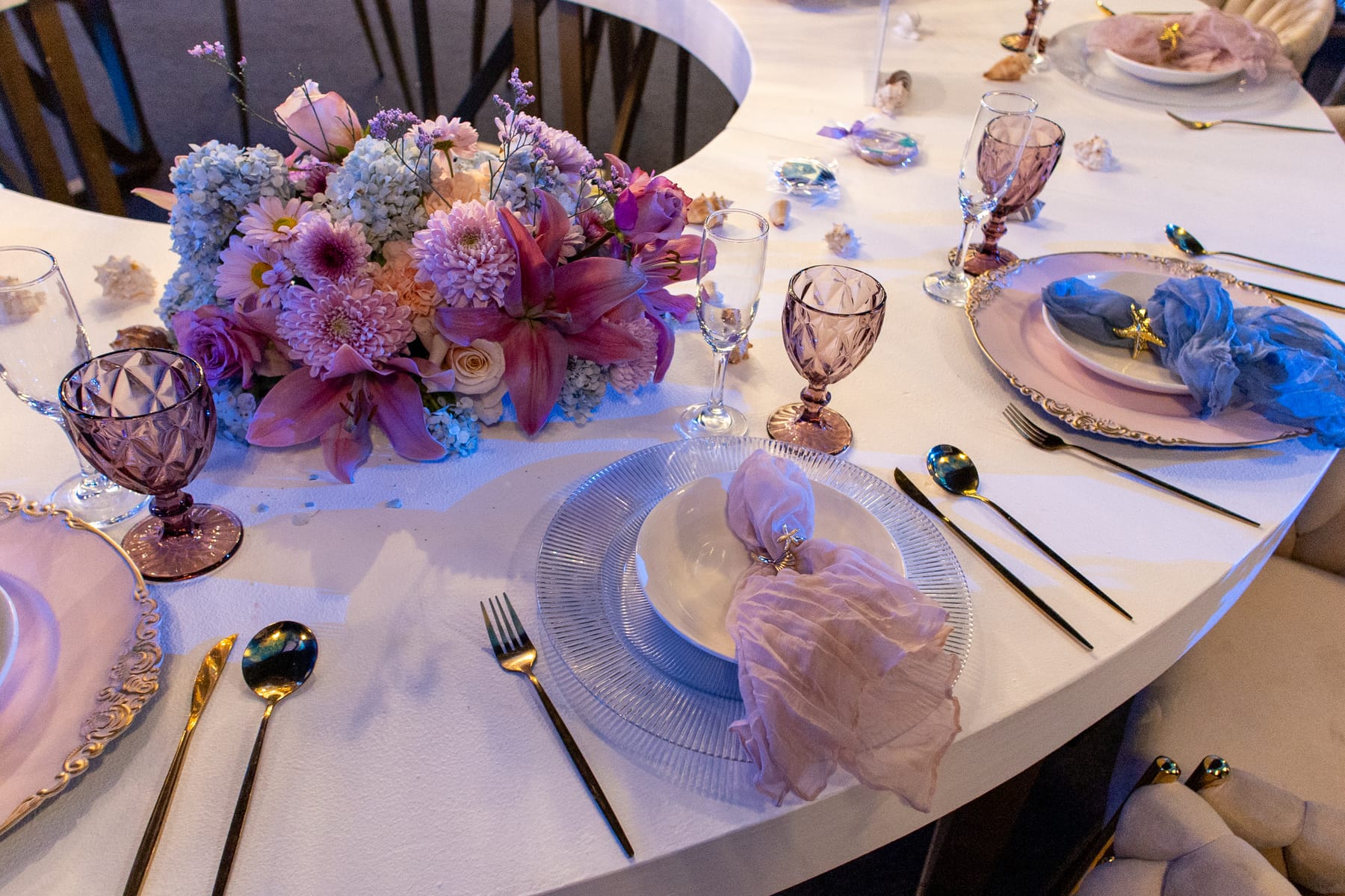 Centro de mesa de flores lila y rosa con copas violeta y vajilla blanca