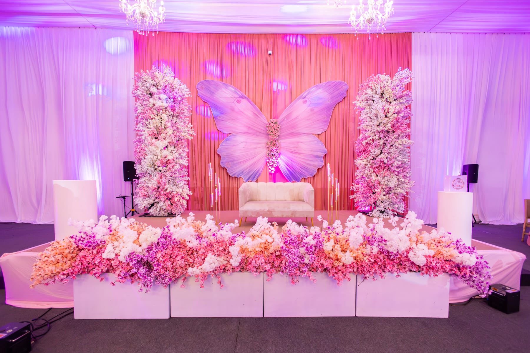 Escenario rosa con mariposa monumental, columnas de flores y mesa principal