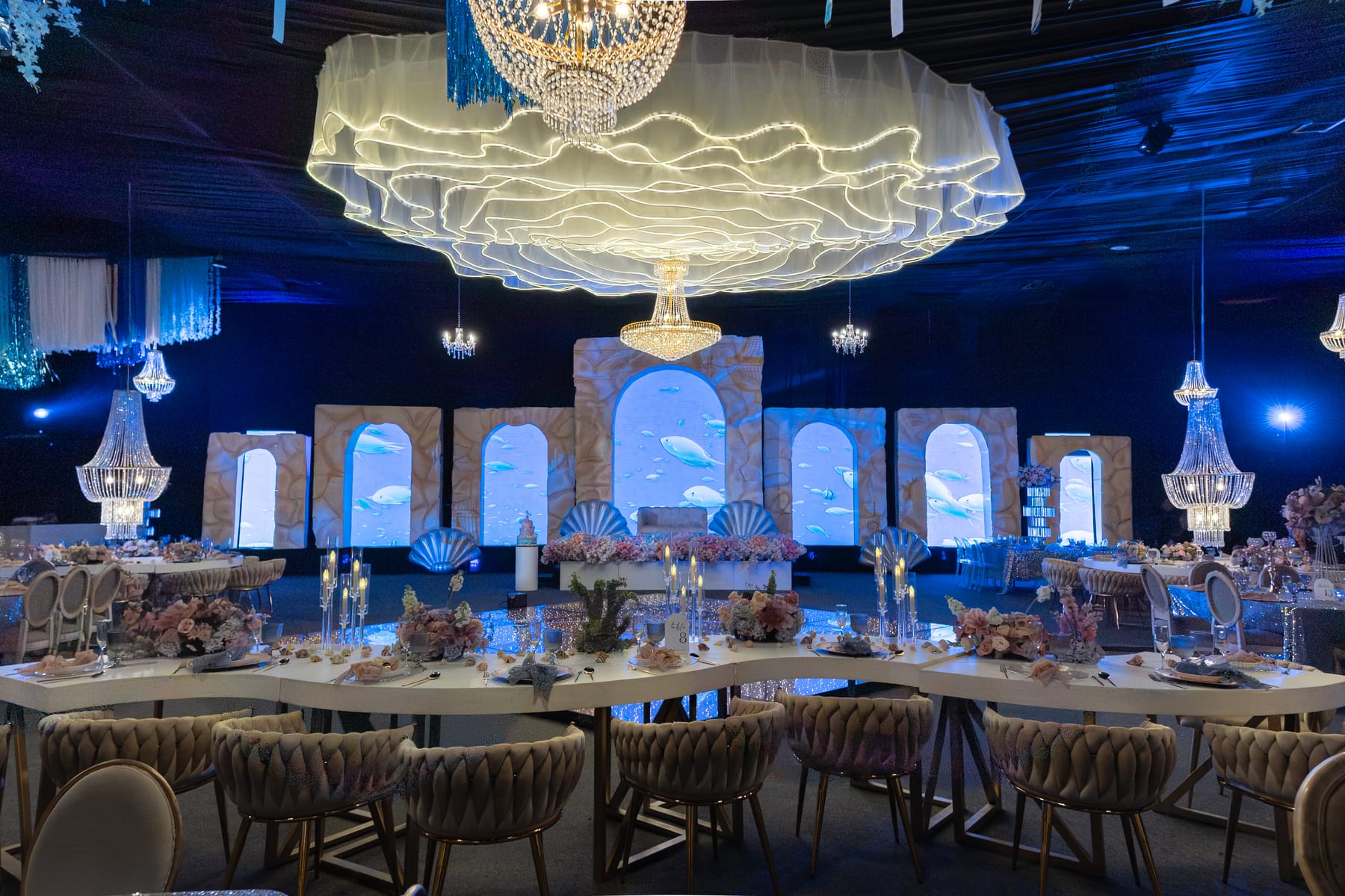 Salón con arcos iluminados en azul, escultura de olas y mesas montadas