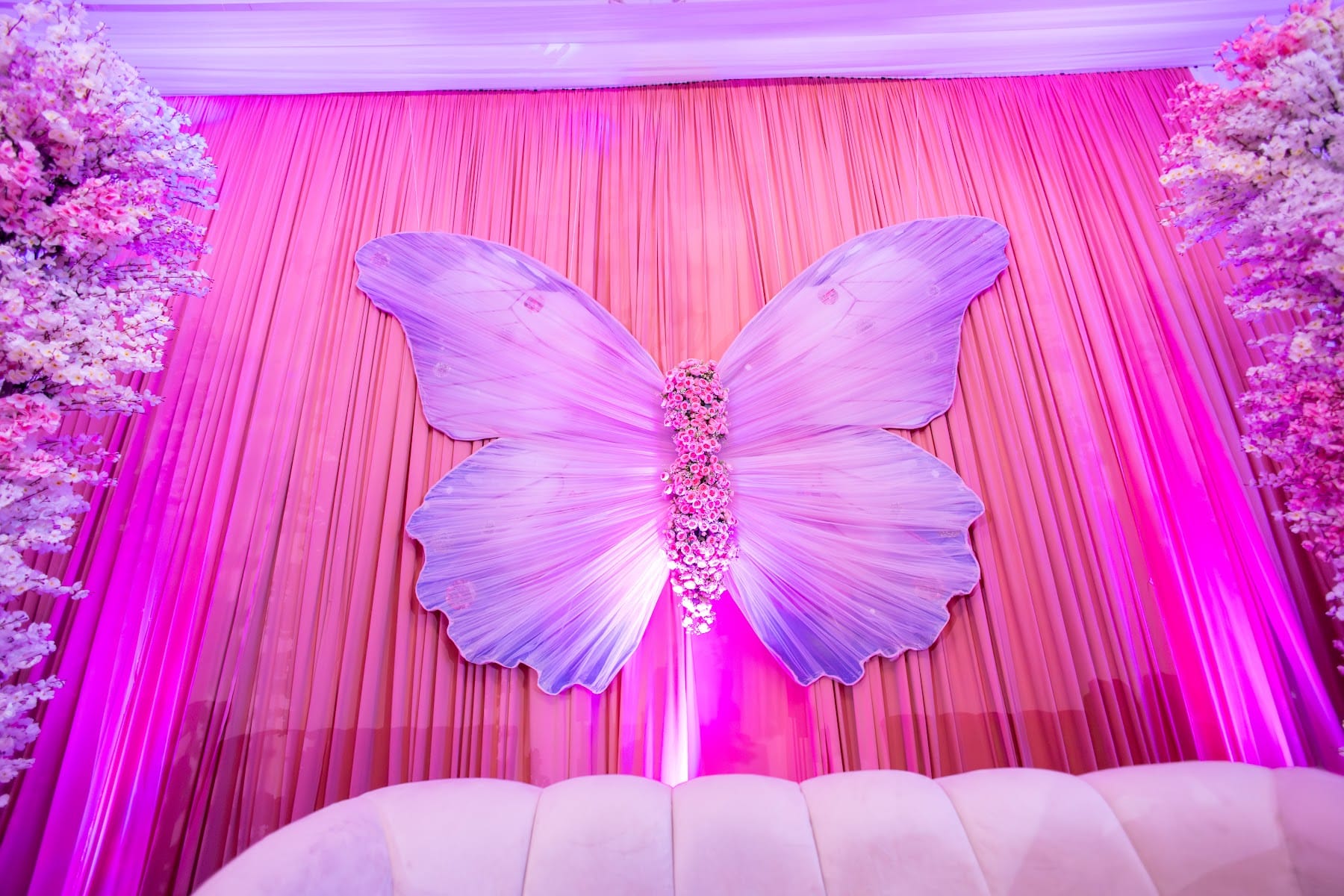 Escenografía de mariposa monumental sobre cortinas iluminadas en rosa