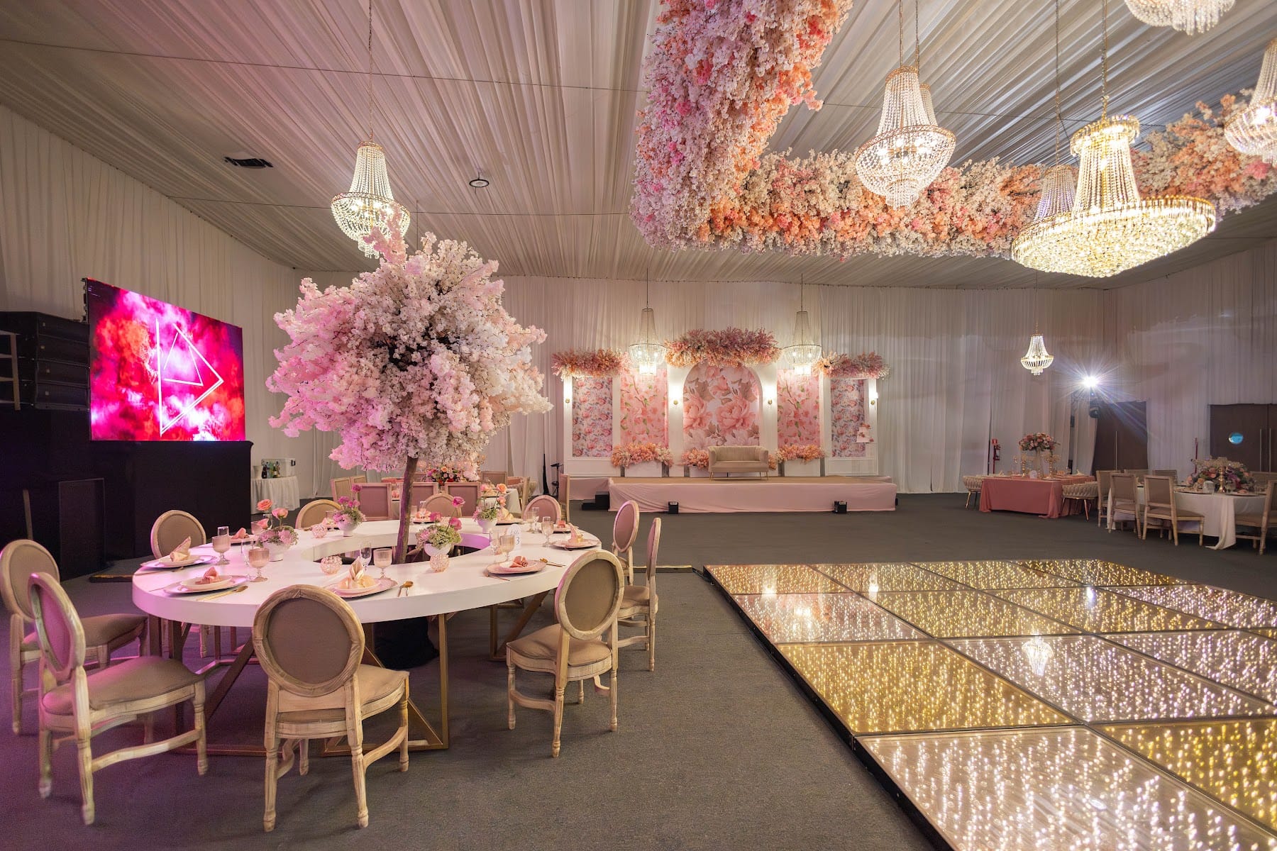 Mesa redonda con árbol de flores rosas junto a la pista de luces para los XV años de Lupita