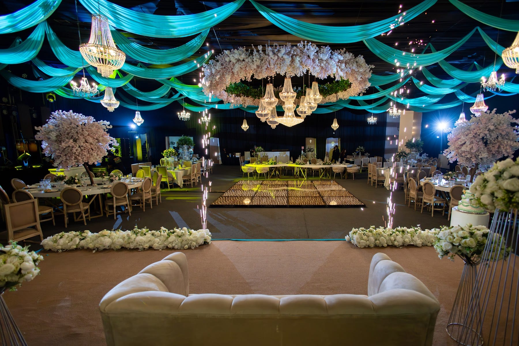 Pista iluminada con sala lounge blanca, árboles de flores y telas esmeralda