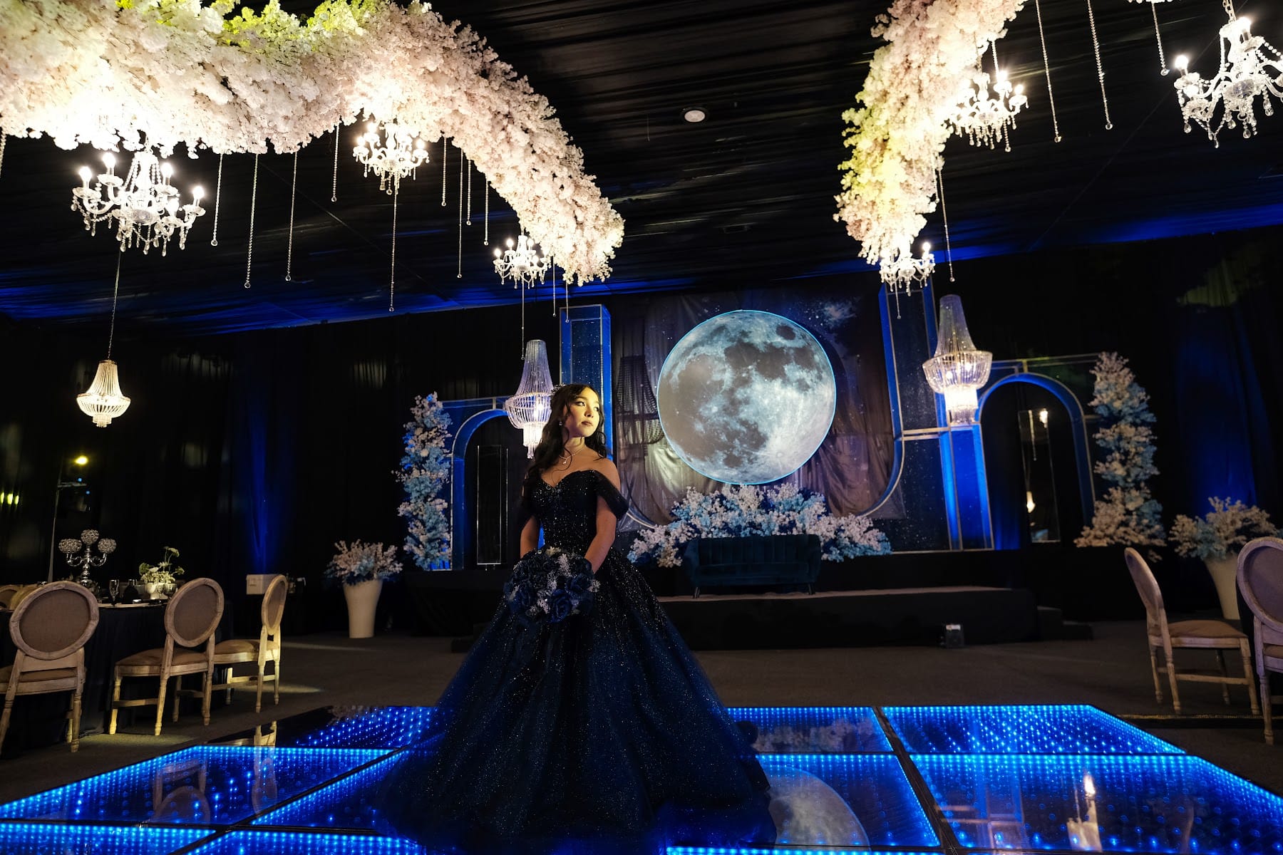 Quinceañera con vestido azul frente a una luna gigante sobre la pista iluminada