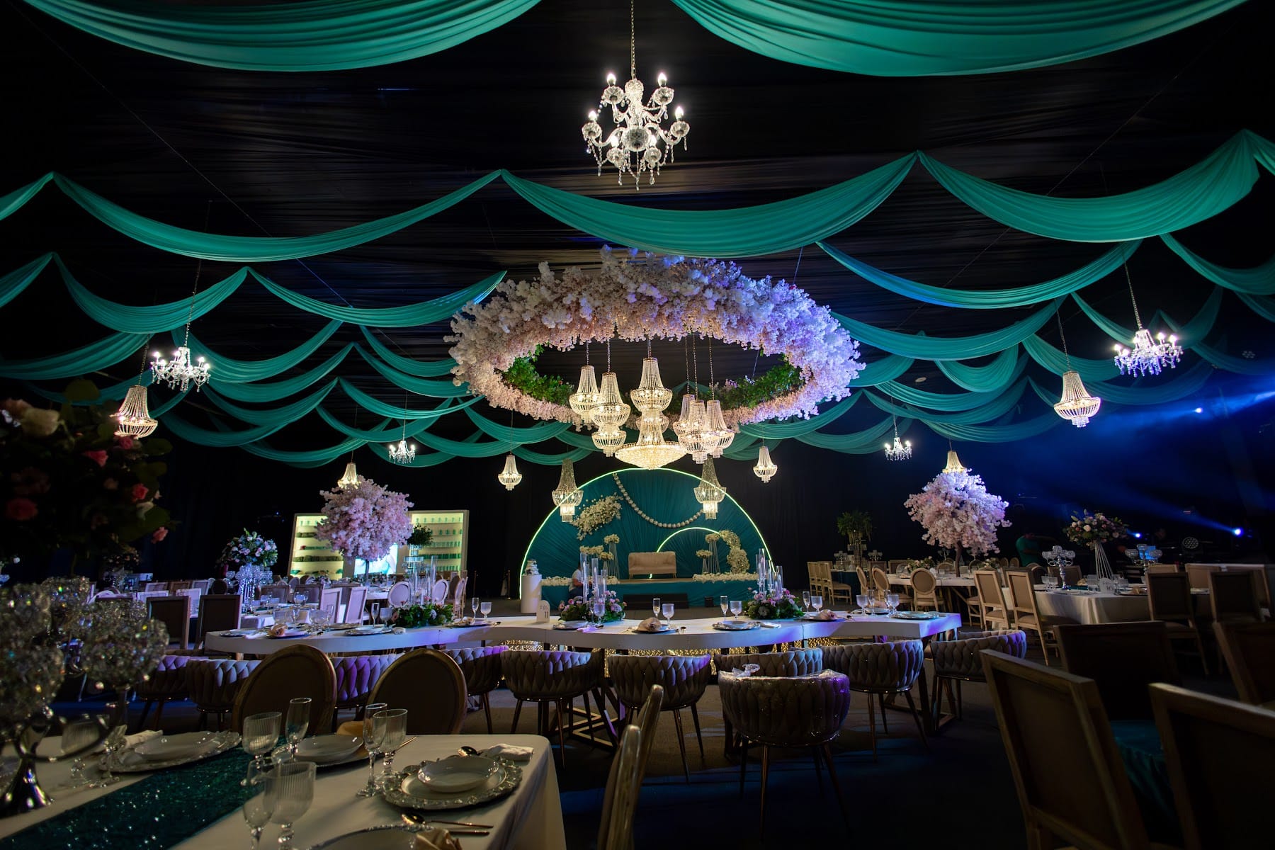 Salón con telas esmeralda, anillo floral y mesas blancas para los XV años de Isabel
