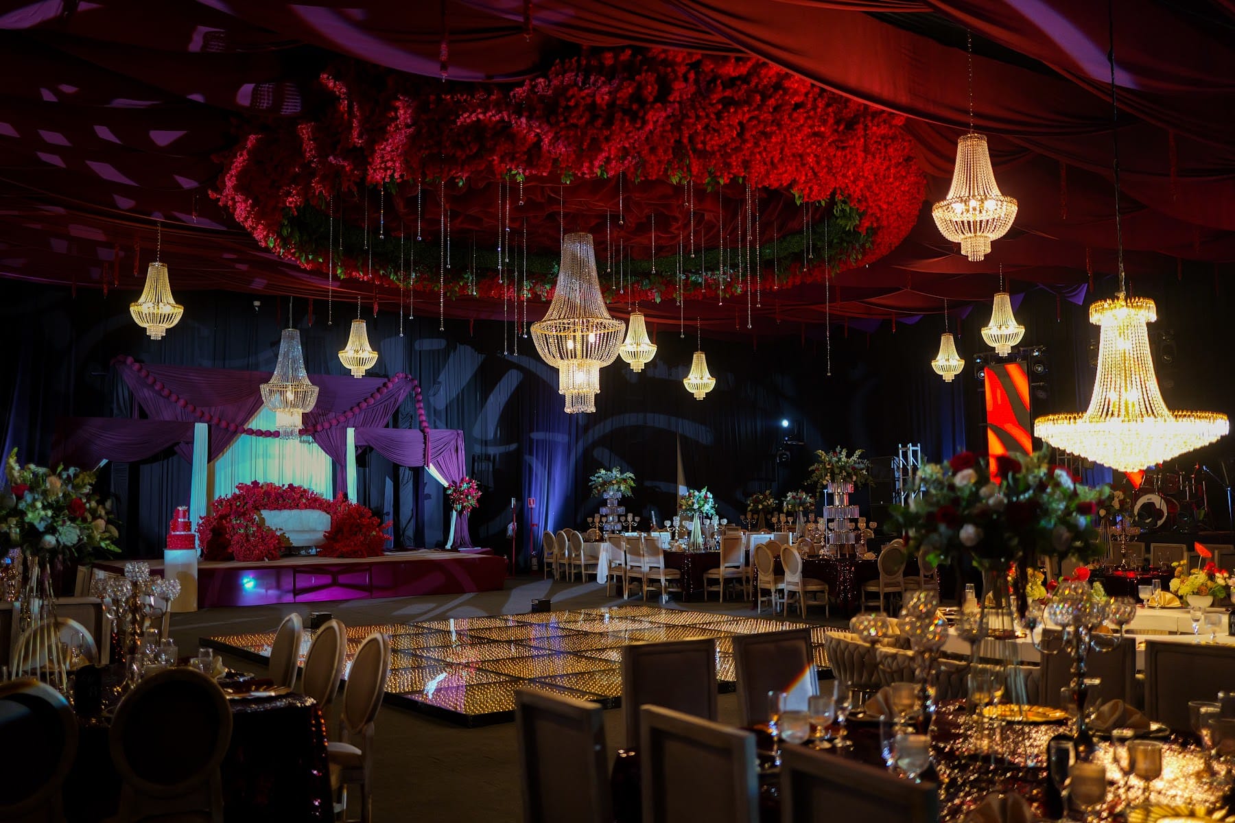 Salón de XV años con techo de flores rojas, candiles de cristal y pista iluminada