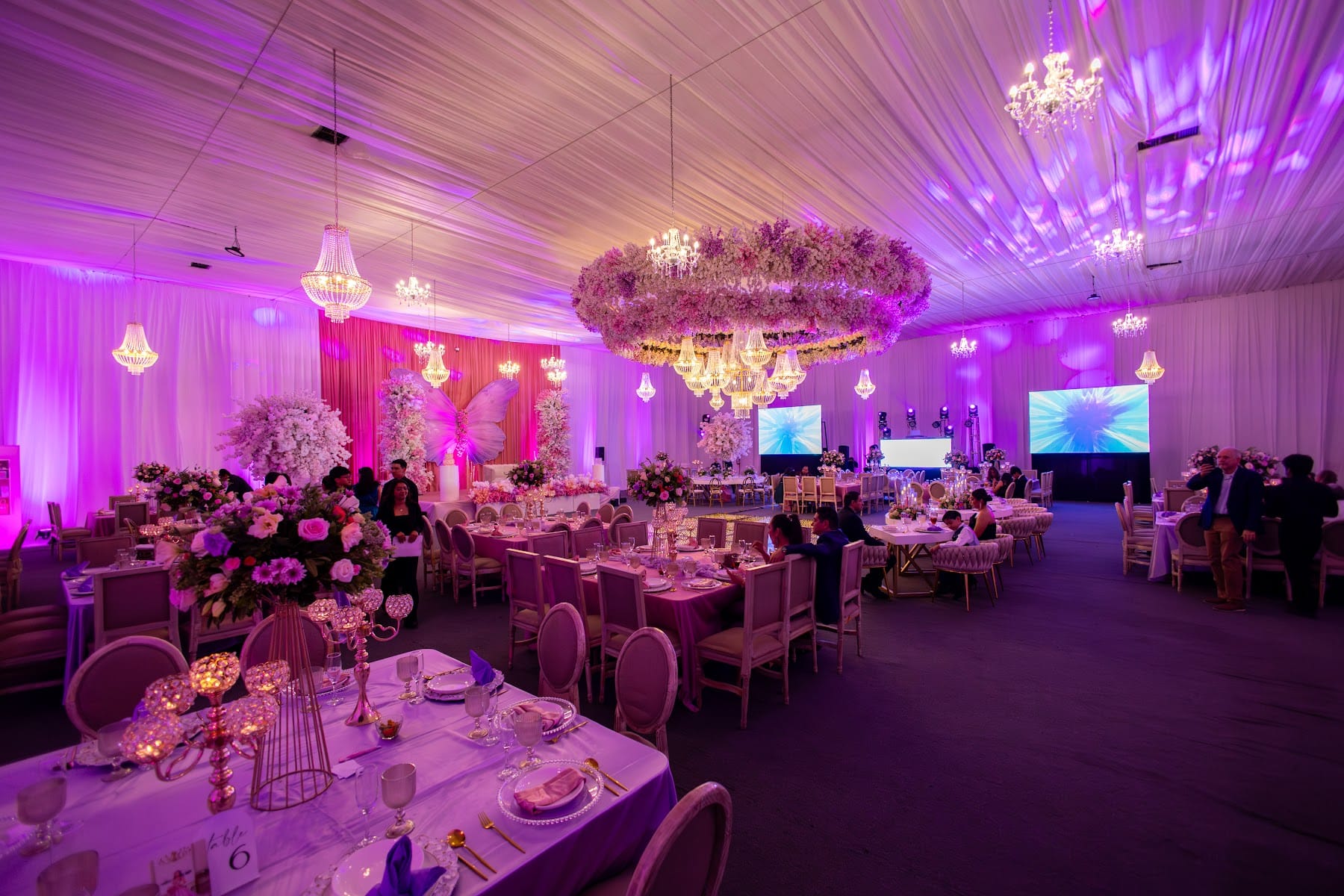 Salón en luz violeta con anillo de flores y candiles sobre las mesas de los XV años de Kristell